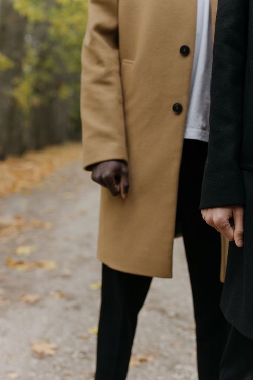 Free Close-up of two individuals in stylish coats walking on a leaf-lined pathway, capturing the essence of autumn fashion. Stock Photo