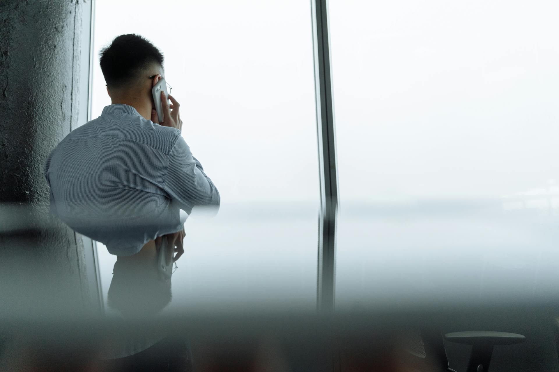 A professional making a phone call in a modern office setting with a city view.