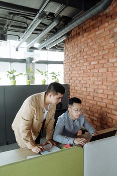 Two men collaborating at a desk in a stylish office with a brick wall backdrop.