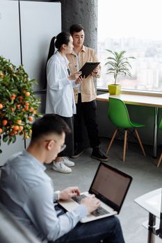 Team engaging in discussion and work in a modern office space with laptops and tablets.