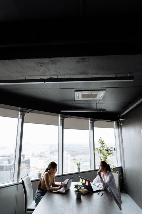 Free Two women engaged in a business meeting inside a modern office with city views. Stock Photo