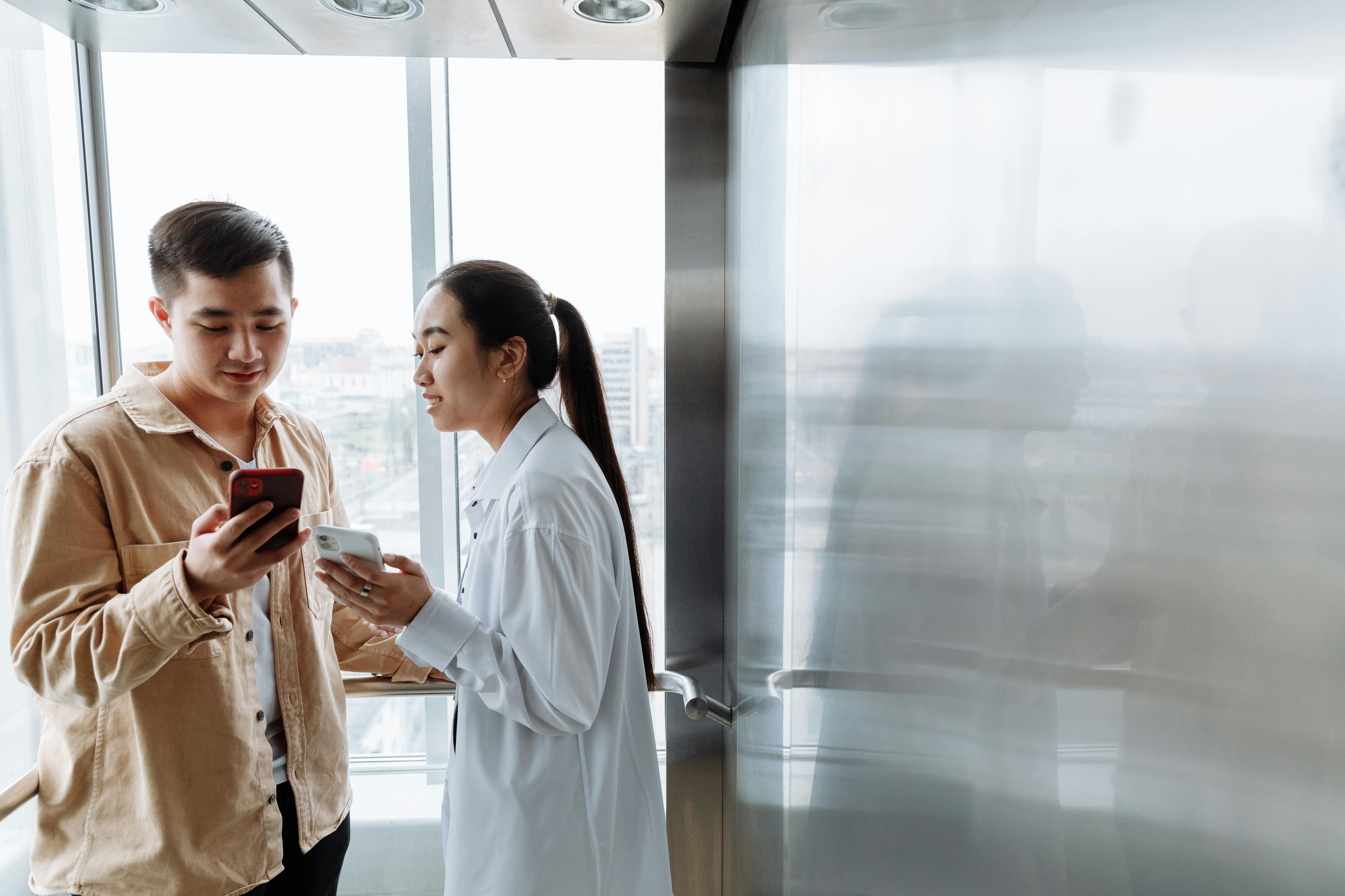 Two professionals using smartphones inside a modern elevator.