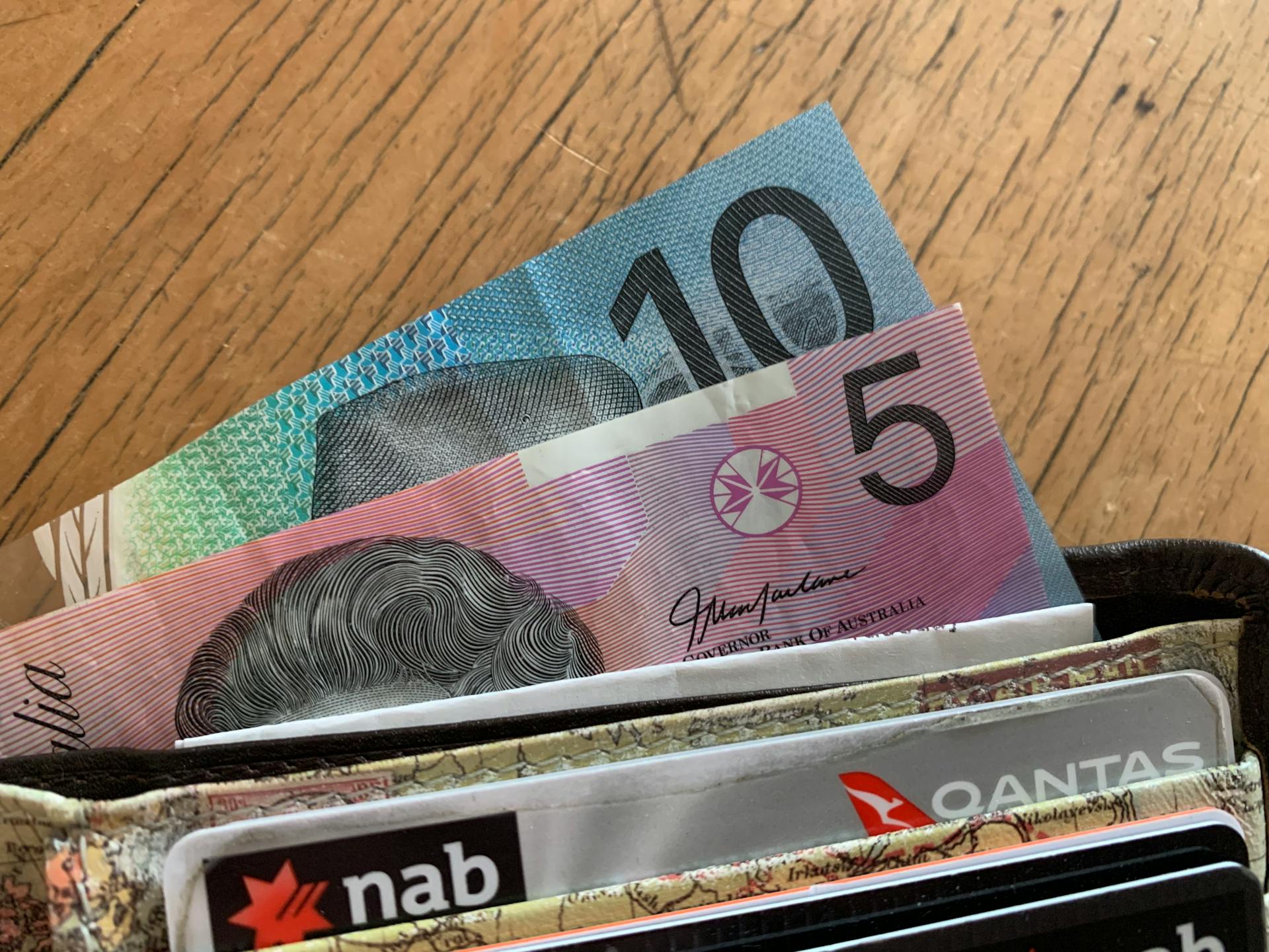 Close-up of Australian dollar bills and credit cards in a wallet on a wooden surface.