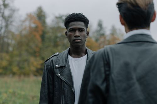 Free A young man wearing a leather jacket stands confidently outdoors with blurred background. Stock Photo