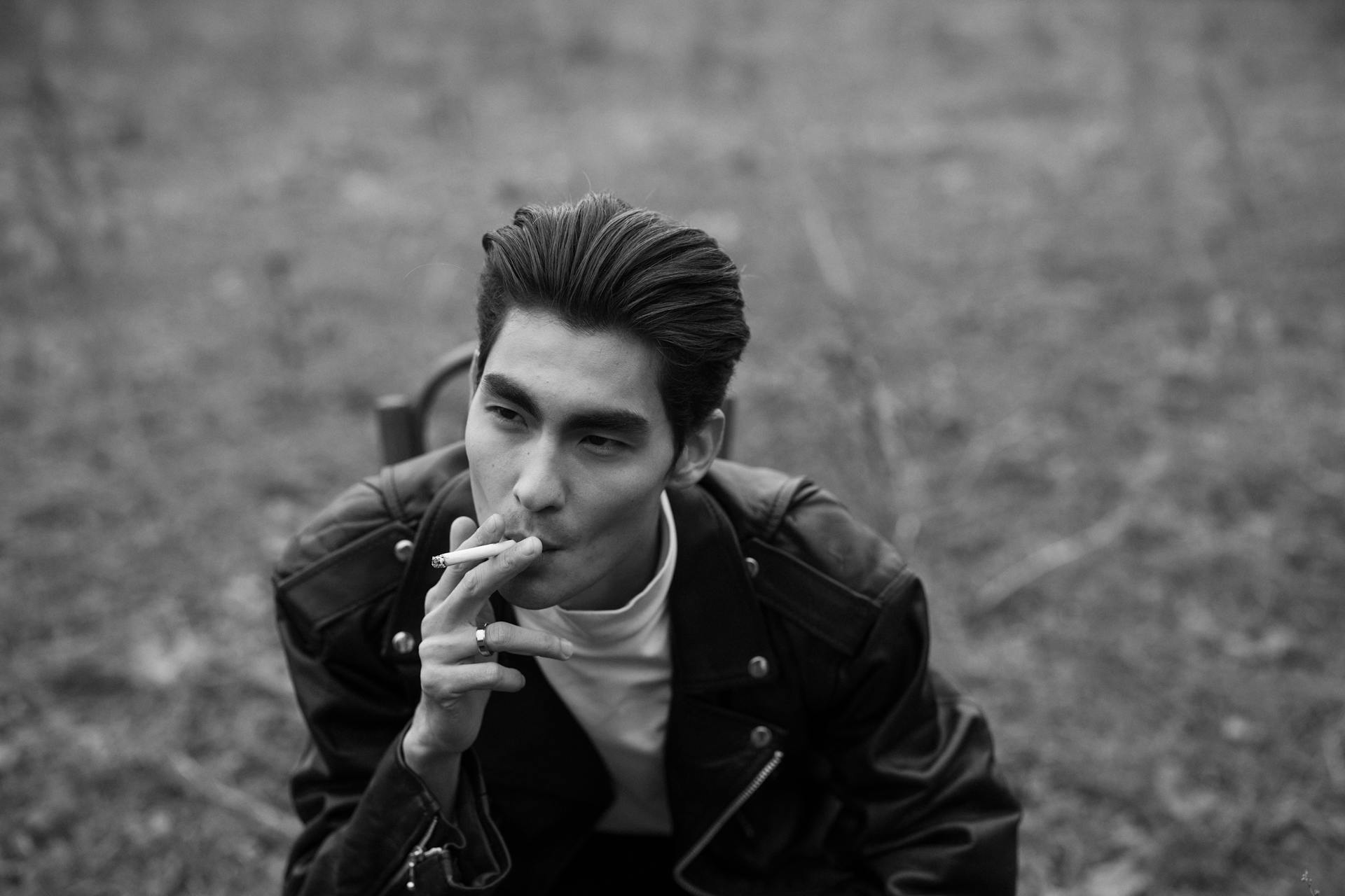 Monochrome portrait of a young man smoking outdoors, conveying a moody and introspective atmosphere.