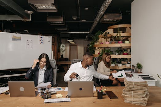 Diverse team collaborating in a modern office setting with laptops and documents.