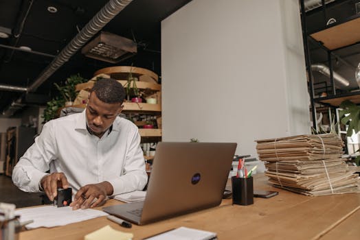 African American man focused on stamping documents at an office desk with a laptop and folders.