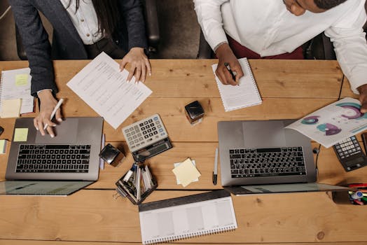 High-angle view of professionals working collaboratively with laptops and documents in an office.