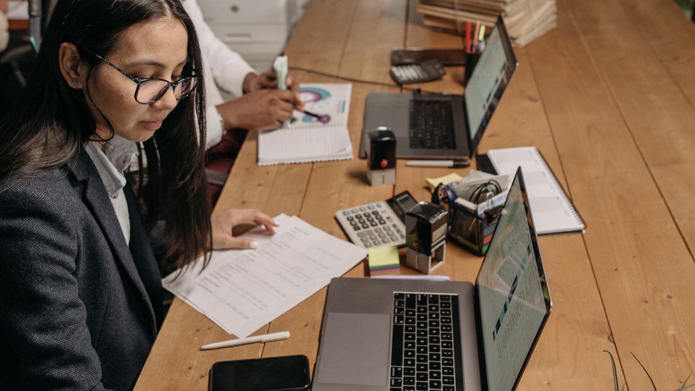 Agree whether a shared workbook contains a snapshot or a query that must refresh. Photo: Pavel Danilyuk / Pexels; stock illustration, not an author test. Two colleagues working with laptops, paper documents and a calculator at an office table