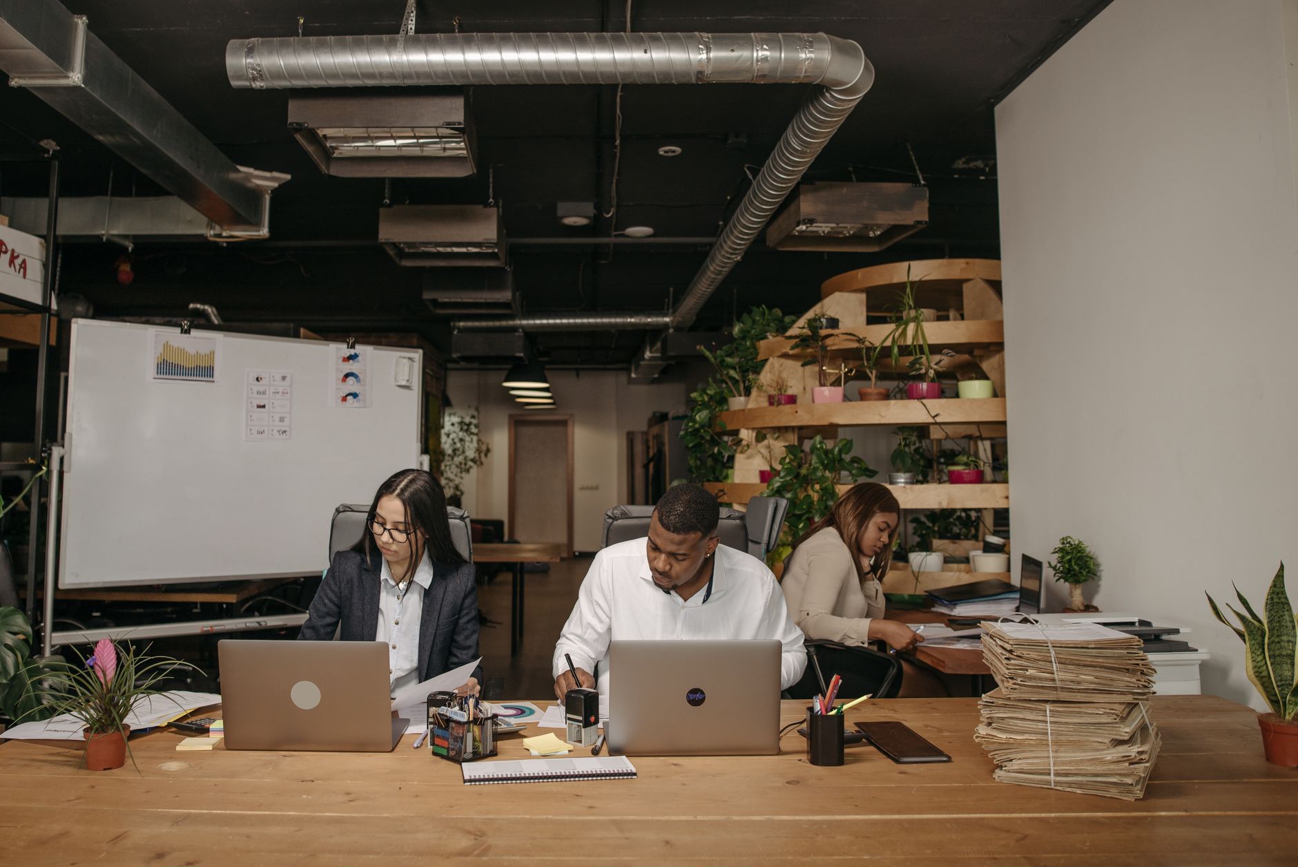 Three professionals focused on work in a stylish office with laptops and documents.