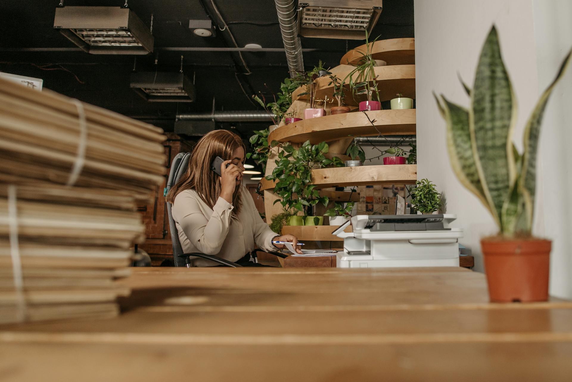 A woman making a phone call in an eco-friendly office with plants and wooden interiors.