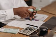Hands counting euro bills on a wooden desk with calculator, financial documents, and laptop nearby.