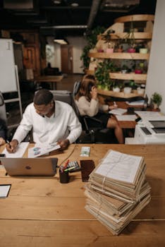 Busy office scene with professionals working on paperwork and laptops, focusing on productivity.