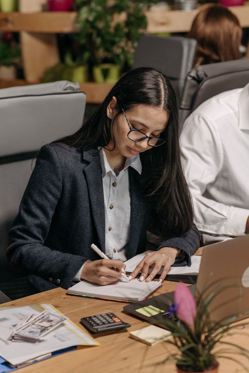 Free Young woman focused on writing notes at her desk in an office setting. Stock Photo