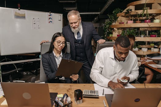 A diverse group of professionals working in a modern office with laptops and documents.