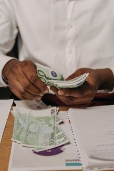 Close-up of hands counting Euro bills with paperwork on a desk.