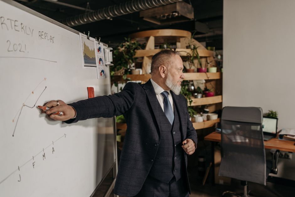 Um empresário de terno apresenta um relatório trimestral em um quadro branco em um ambiente de escritório moderno.