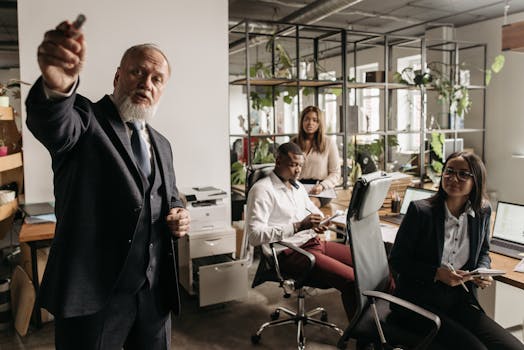 A diverse team in a modern office setting engaged in a business meeting with a senior leader presenting.