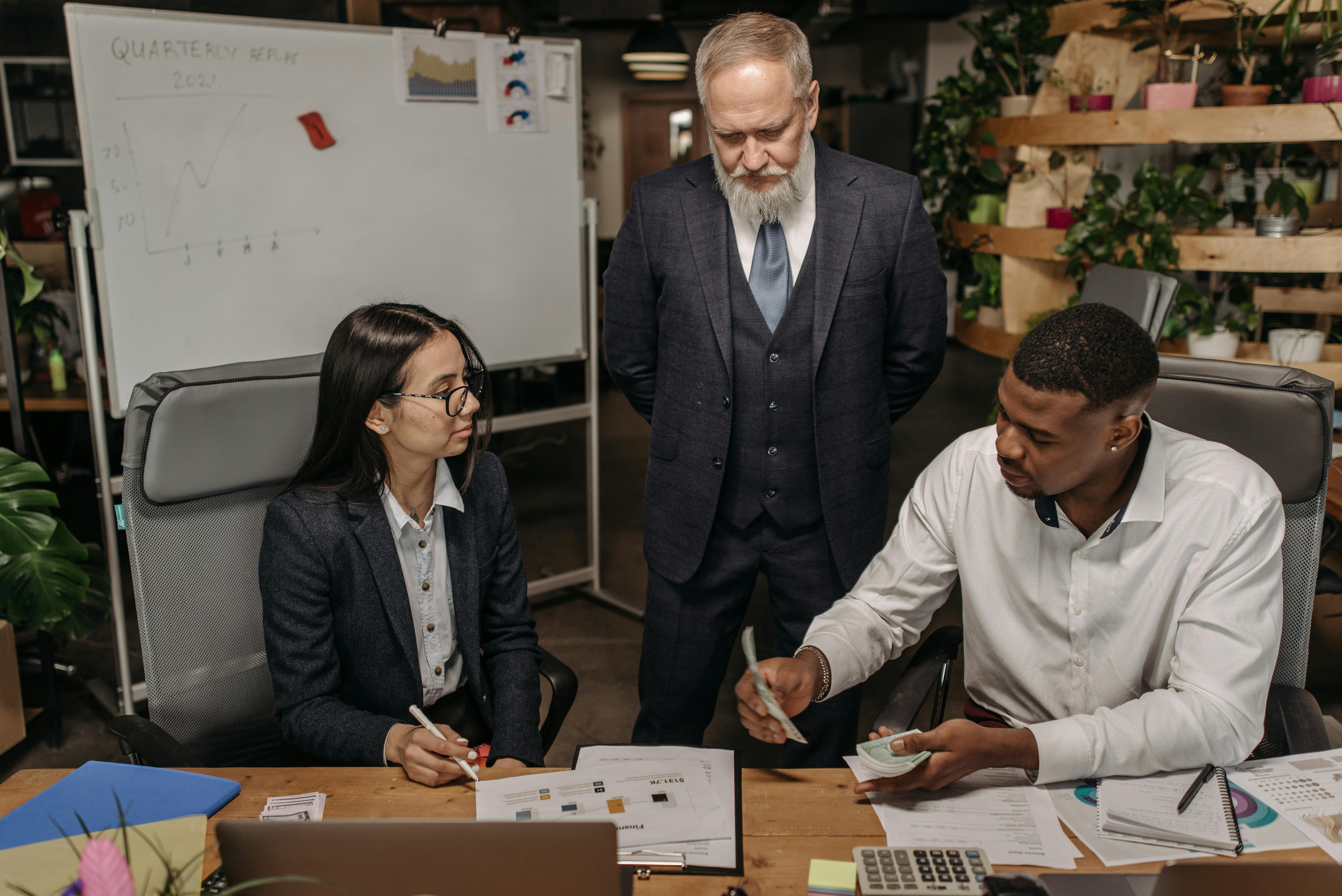 Three business professionals discussing reports at an office desk