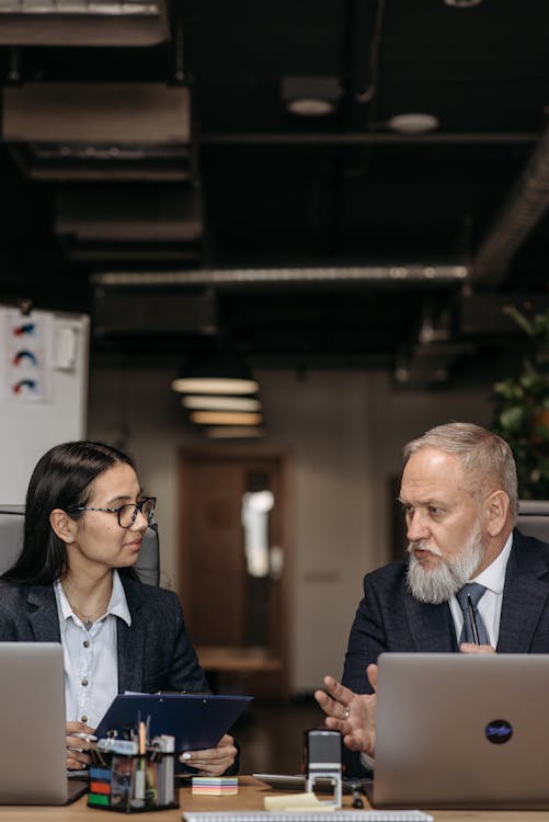 Free Business leaders collaborating in a modern office setting, discussing on laptops. Stock Photo Free Business leaders collaborating in a modern office setting, discussing on laptops. Stock Photo