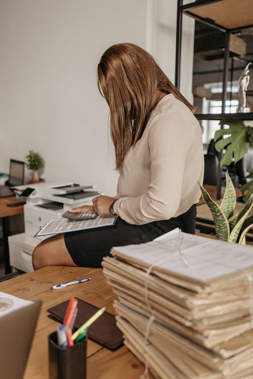 Woman Sitting on a Wooden Desk Using a Calculator