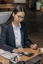 A Woman in a Blazer and Eyeglasses Using a Calculator