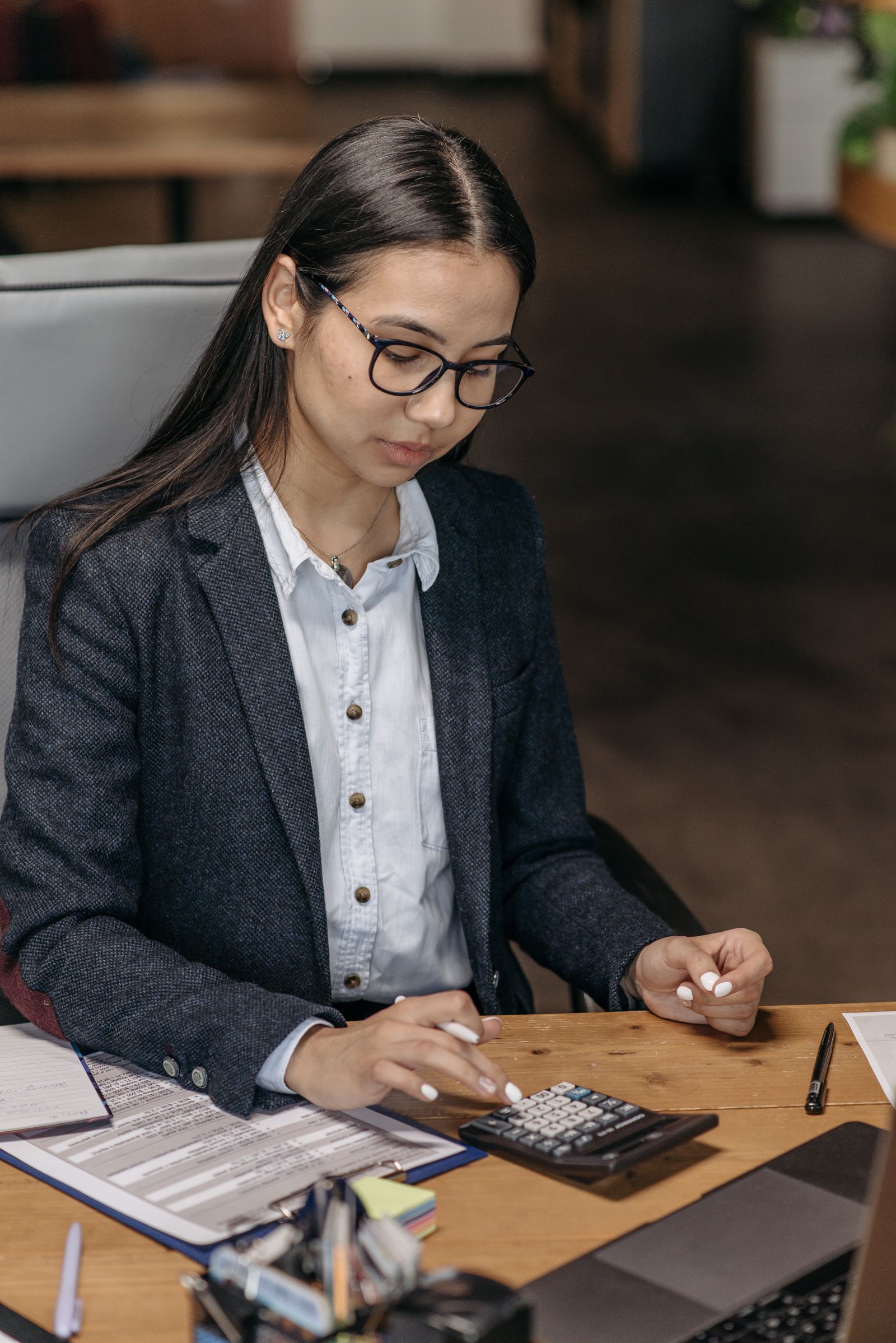 Free Professional Asian woman in a blazer using calculator at desk, calculating finances. Stock Photo