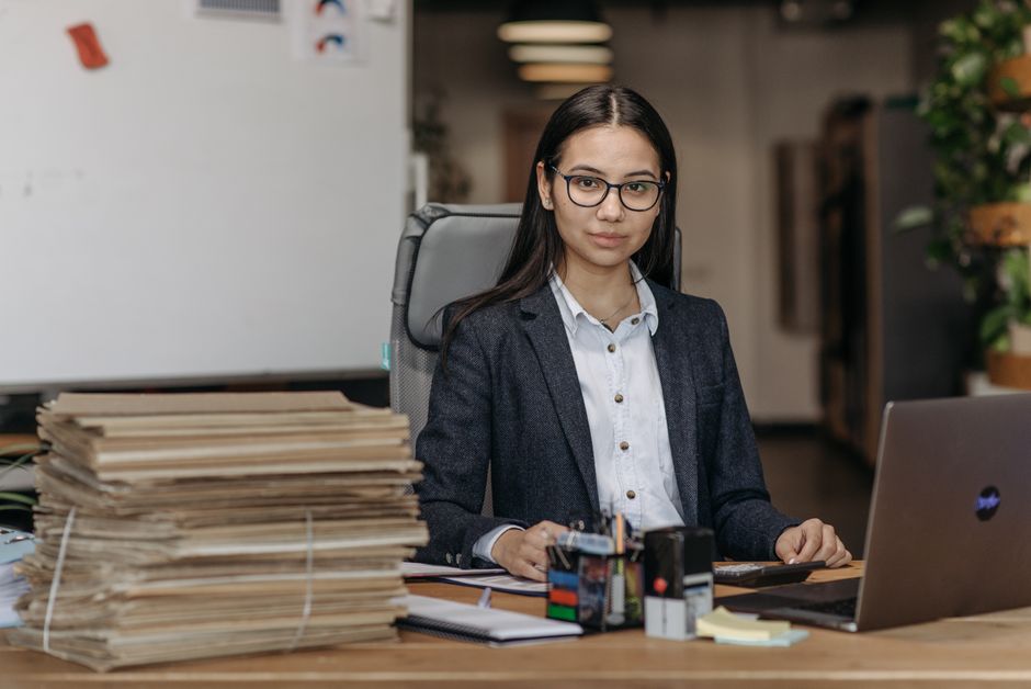 Mujer segura de sí misma con gafas trabajando en un entorno de oficina moderno.
