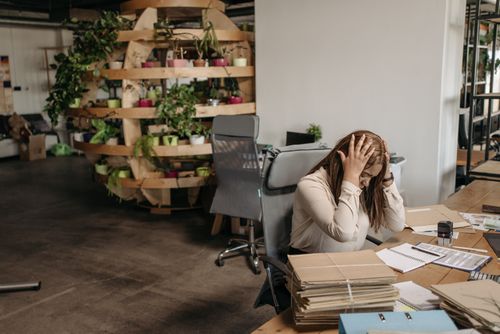 Free A stressed woman sits overwhelmed at her desk, surrounded by paperwork in a modern office setting. Stock Photo