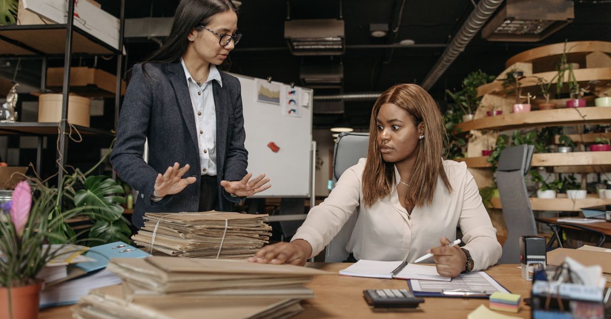 Two businesswomen in corporate attire working together in a modern office setting with documents.