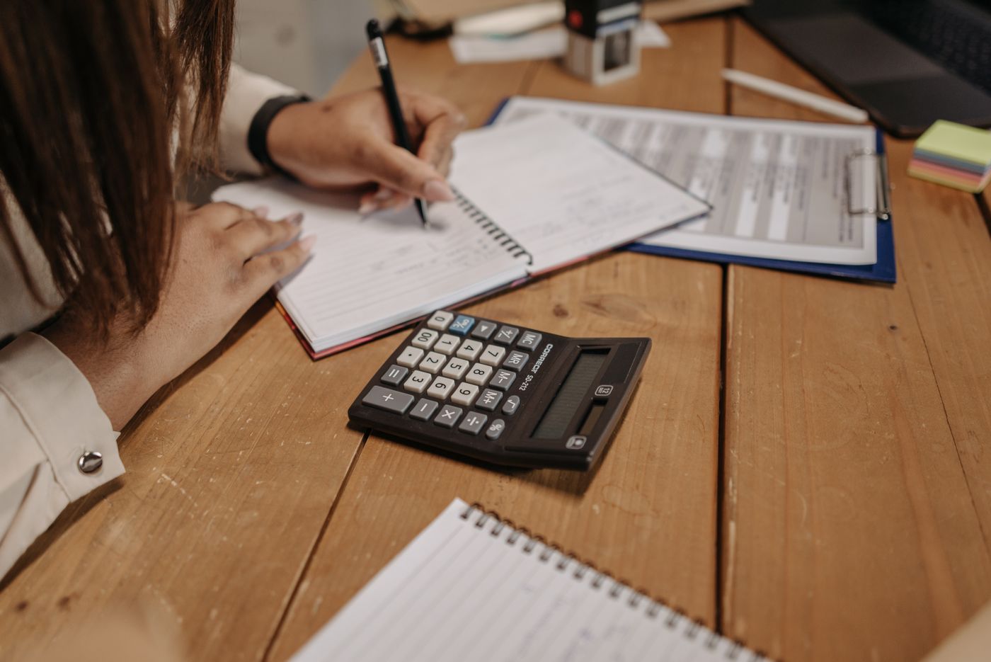 A woman's hands writing notes in an open journal at a wooden desk