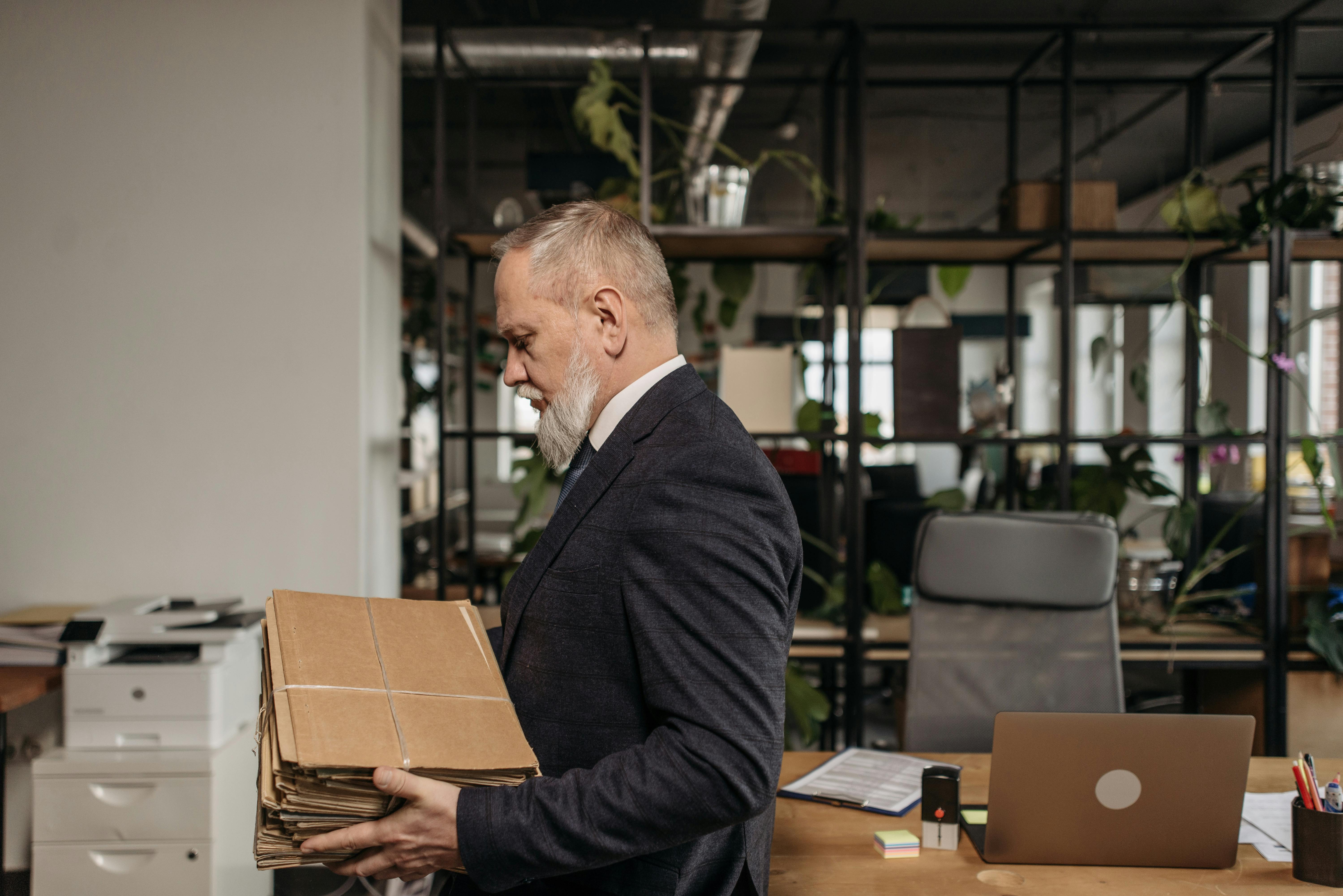 Senior businessman in office attire organizing a stack of documents in a modern office setting.