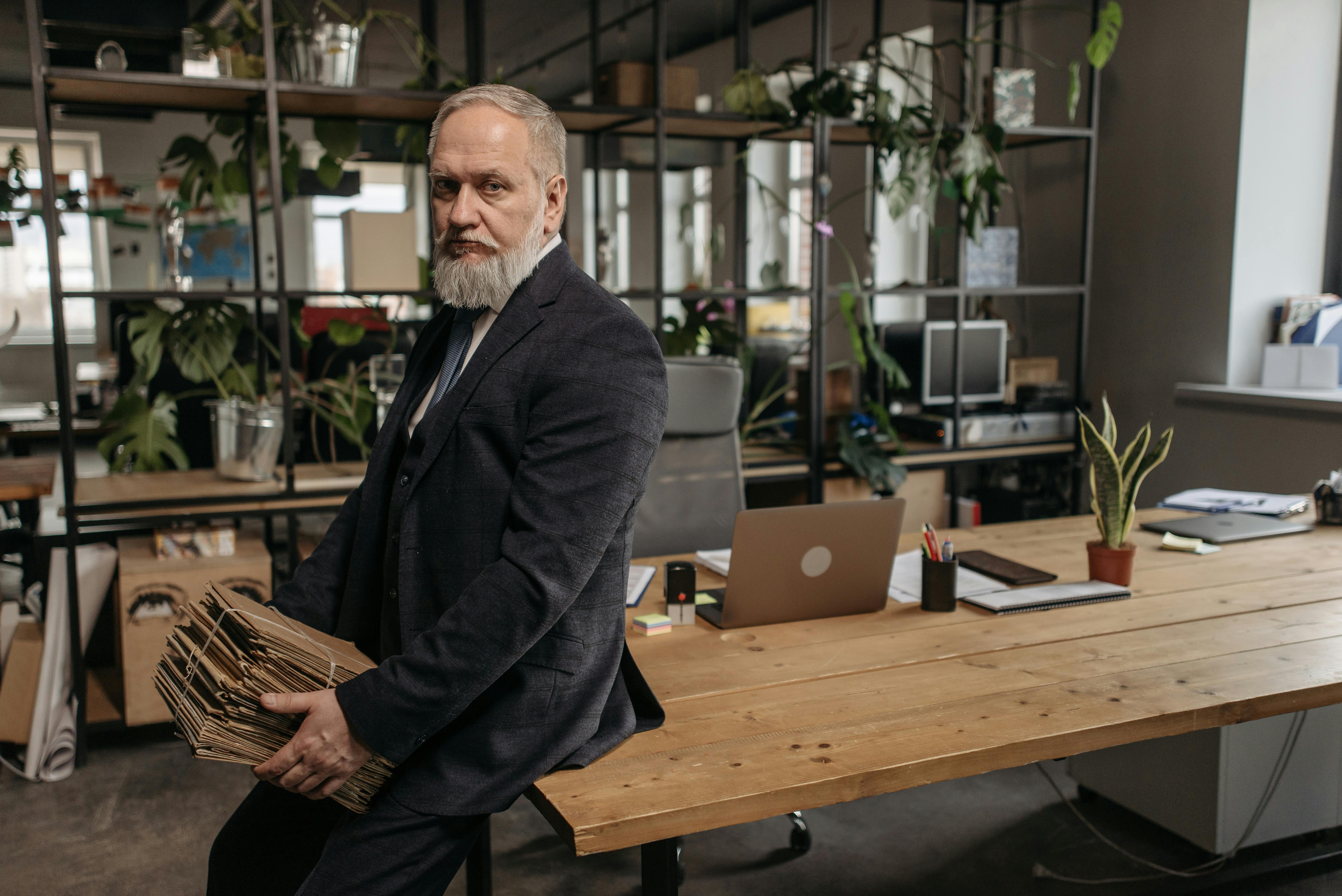 elderly man in black suit sitting on wooden table while carrying brown folders