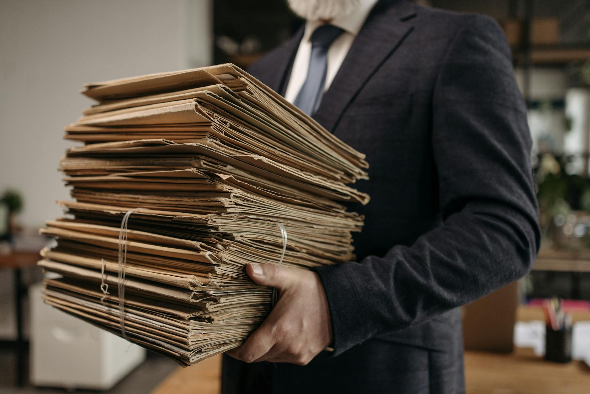 Close-up of business professional holding a large stack of brown folders in an office setting.