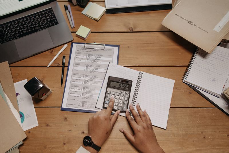 Hands working with calculator and documents on wooden desk in office setting.