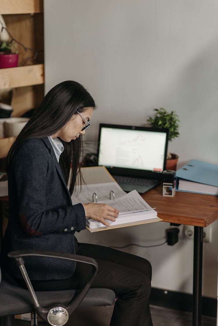 Young Woman Sitting At The Desk In An Office And Looking At Documents 