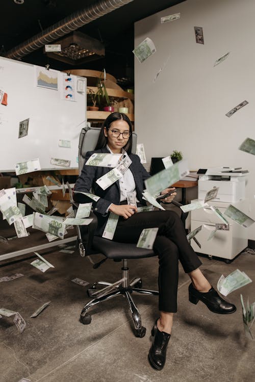 Woman Sitting on an Office Chair with Money Flying All Around Her 