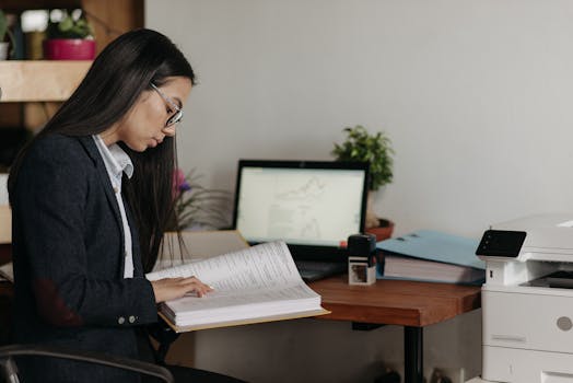 Woman reading documents at office desk with computer and printer.
