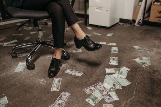 Person sitting on a chair with scattered banknotes on a concrete office floor.