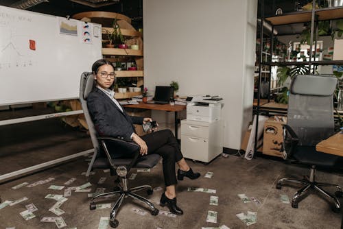 Free A Woman in Business Attire Sitting at the Office with Banknotes on the Floor Stock Photo