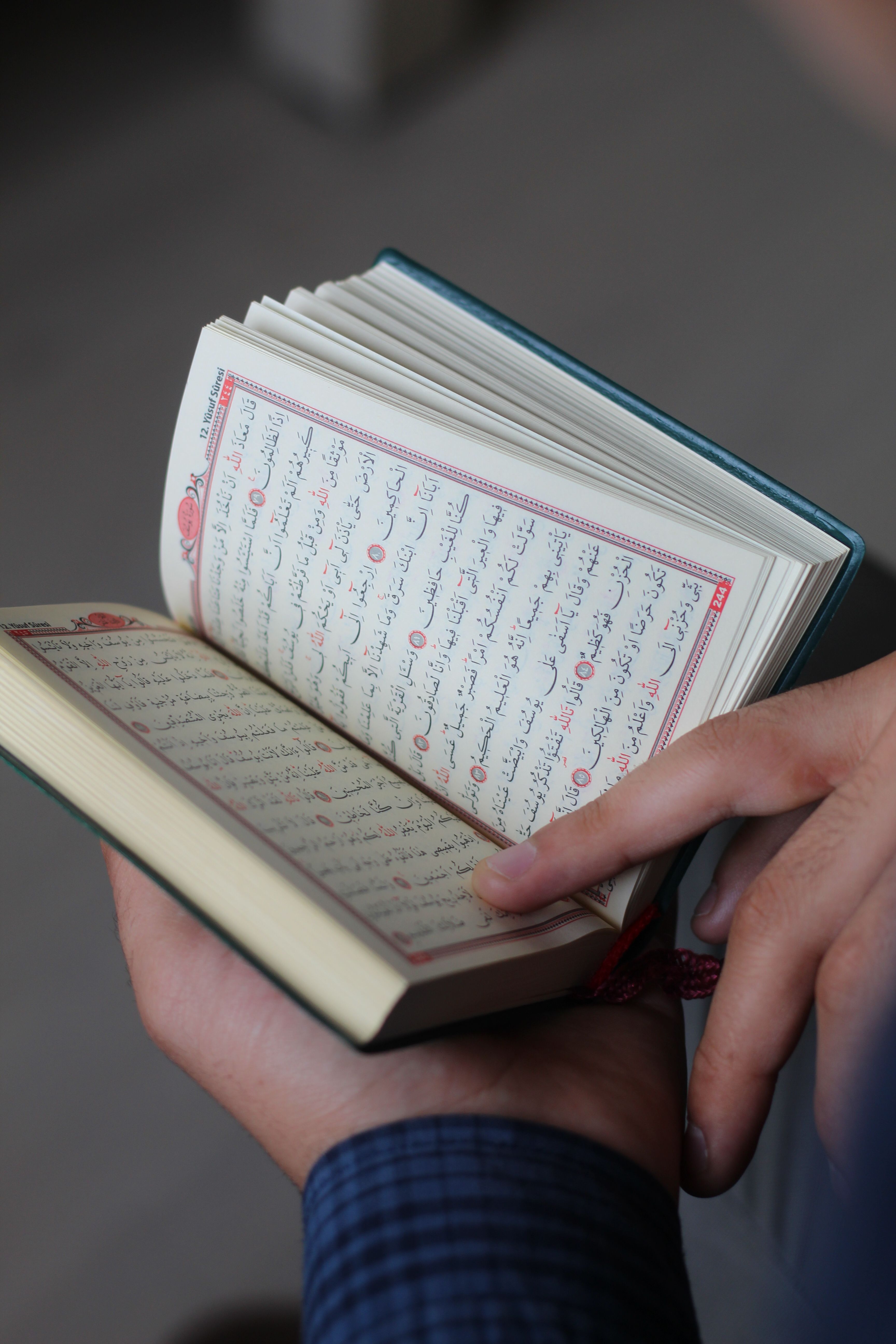 A close-up shot of hands holding and reading the Quran indoors.