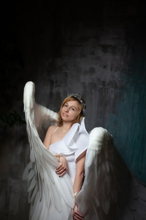 Free A woman in angel wings poses gracefully against a textured wall, exuding ethereal elegance. Stock Photo