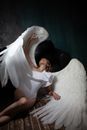 From above of young blond female wearing angel costume lying on floor in dark room and looking up