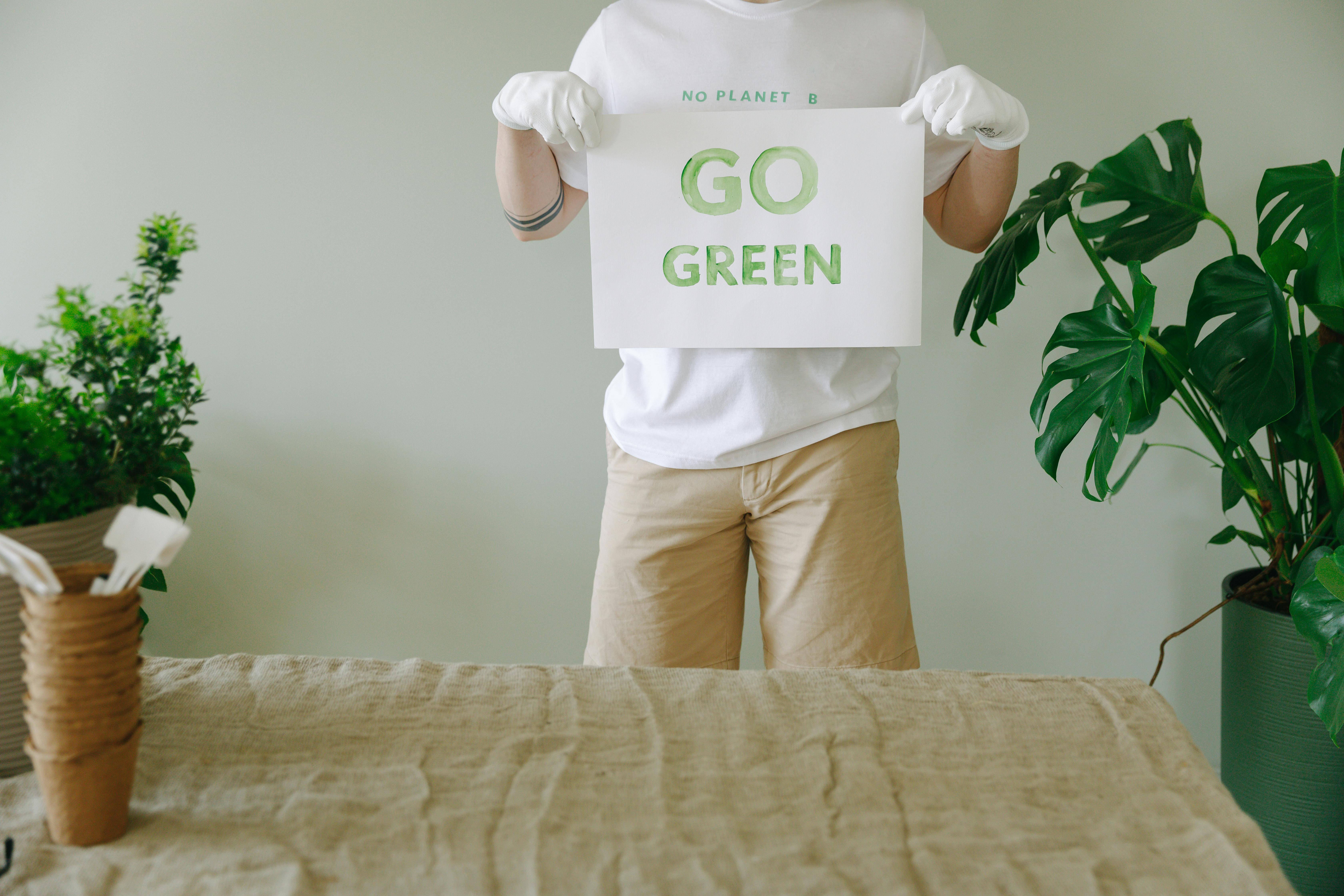 A person holding a 'Go Green' sign promoting environmental awareness indoors.