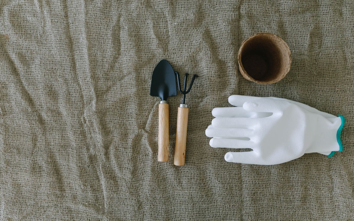 Flat lay of gardening tools, gloves, and pot on burlap surface.