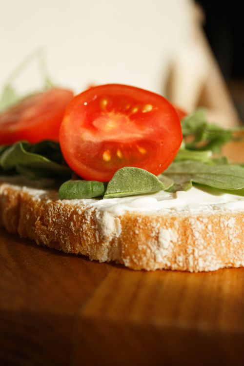 Free Close-up of a fresh bread sandwich with tomatoes, spinach, and cheese on a wooden surface. Stock Photo