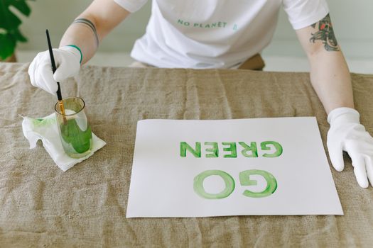 Person painting eco-friendly 'Go Green' message on paper with gloves and brush.