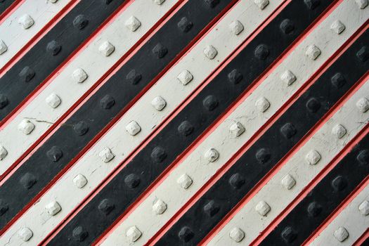 Close-up of a diagonal metal pattern with rivets in red, white, and black stripes.