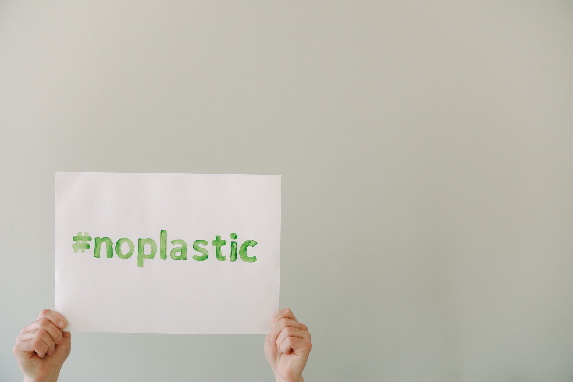 Hands holding a sign with the slogan #noplastic promoting environmental awareness.