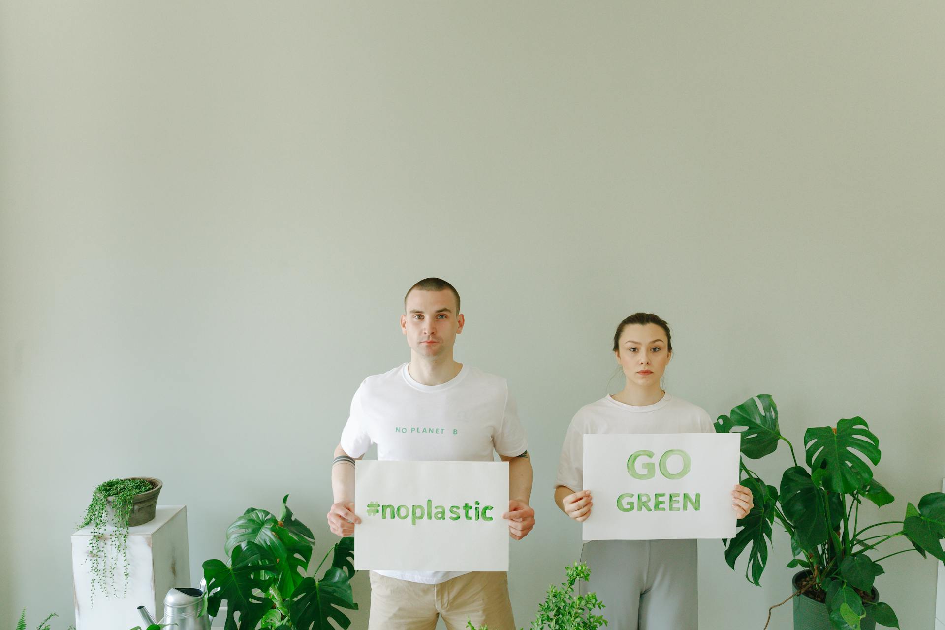 Two people advocating environmental sustainability with signs promoting 'Go Green' and '#NoPlastic'.